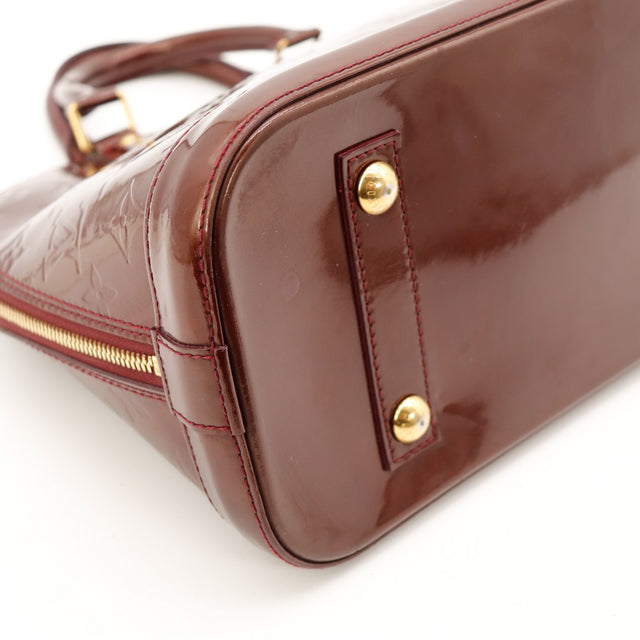 Détail coin inférieur et pieds Louis Vuitton Alma PM Vernis Amarante — AMANA Vintage