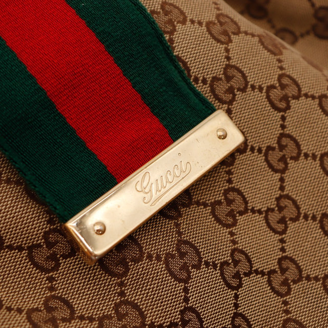 Détail plaque Gucci dorée gros plan bande Web toile monogrammée — AMANA Vintage